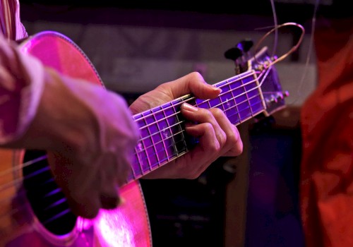 A person is playing an acoustic guitar, focusing on the strings and fingers, with a colorful lighting effect in the background.