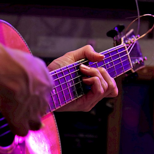 A person is playing an acoustic guitar, focusing on the strings and fingers, with a colorful lighting effect in the background.