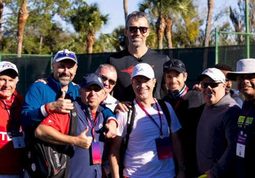 A group of people in sports attire posing outdoors with palm trees in the background, some wearing caps and sunglasses.