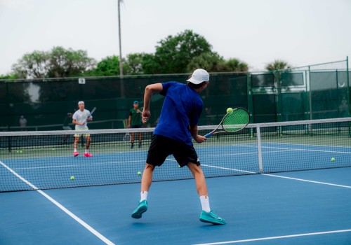 Two people are playing tennis on an outdoor court, with one player preparing to hit the ball.