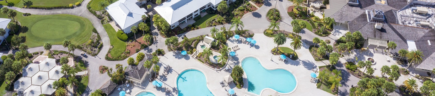 Aerial view of a resort with multiple pools, palm trees, landscaped gardens, and nearby golf course.